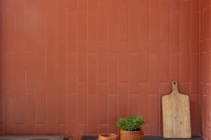 O fogão a lenha marca a área gourmet e reforça o caráter doméstico da casa. Revestimento cerâmico em tom avermelhado reforça a identidade cromática do projeto.